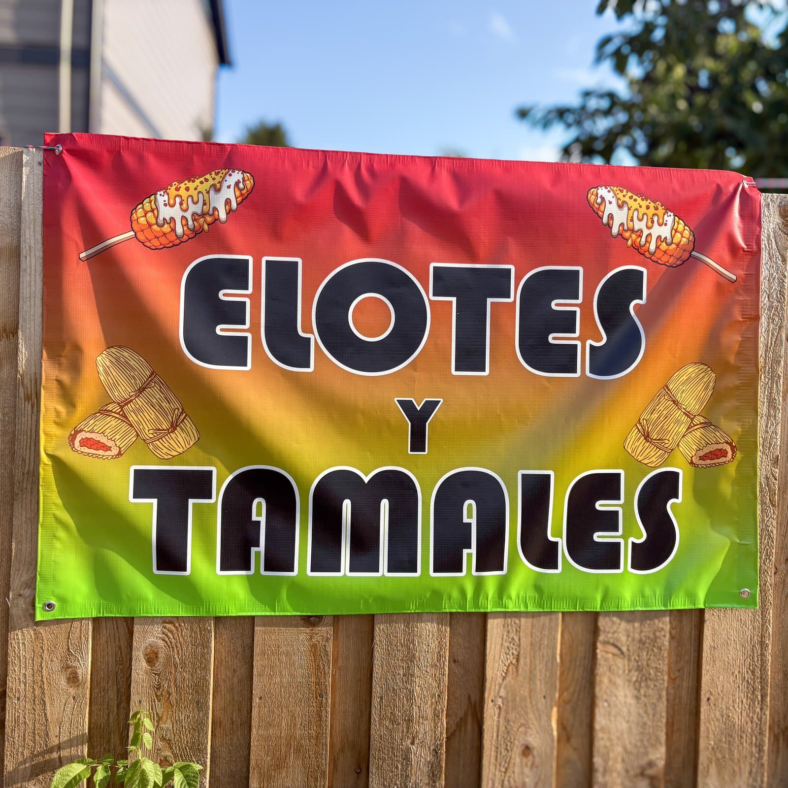 A printed vinyl banner for a food stand, hung on a wooden fence