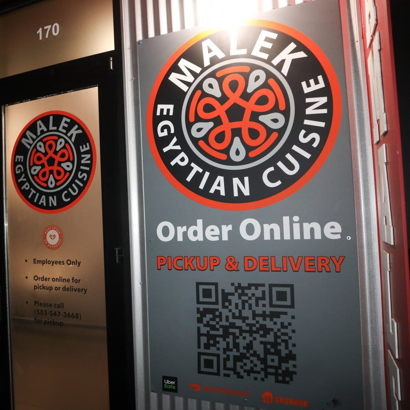 A restaurant entrance at night with printed graphics on the door and a large sign panel beside it